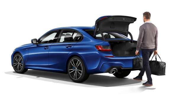 BMW 3 Series Sedan (G20), automatic tailgate operation. Three-quarter rear shot of standing BMW 3 Series Sedan (G20) with driver automatically opening the tailgate with his foot.