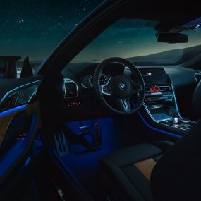 Interior BMW M8 Coupé. BMW M8 Coupé, interior at night with M leather steering wheel and blue ambient light with open driver door.
