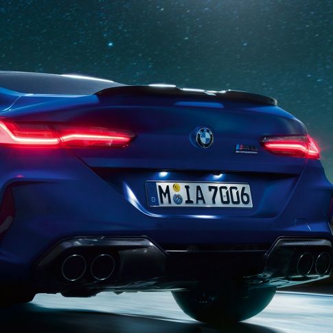 M diffuser in Carbon Black. BMW M8 Coupé in Marina Bay Blue metallic, close-up rear at night with M diffuser in Carbon Black.