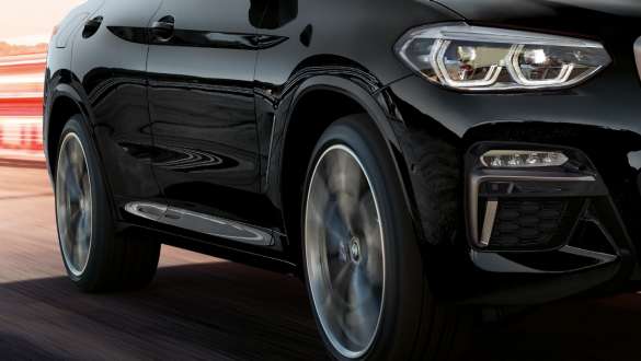 BMW X4 M40i three-quarter side view. BMW X4 M40i in Black Sapphire metallic, driving, exterior, three-quarter side view with rotating light alloy wheels.
