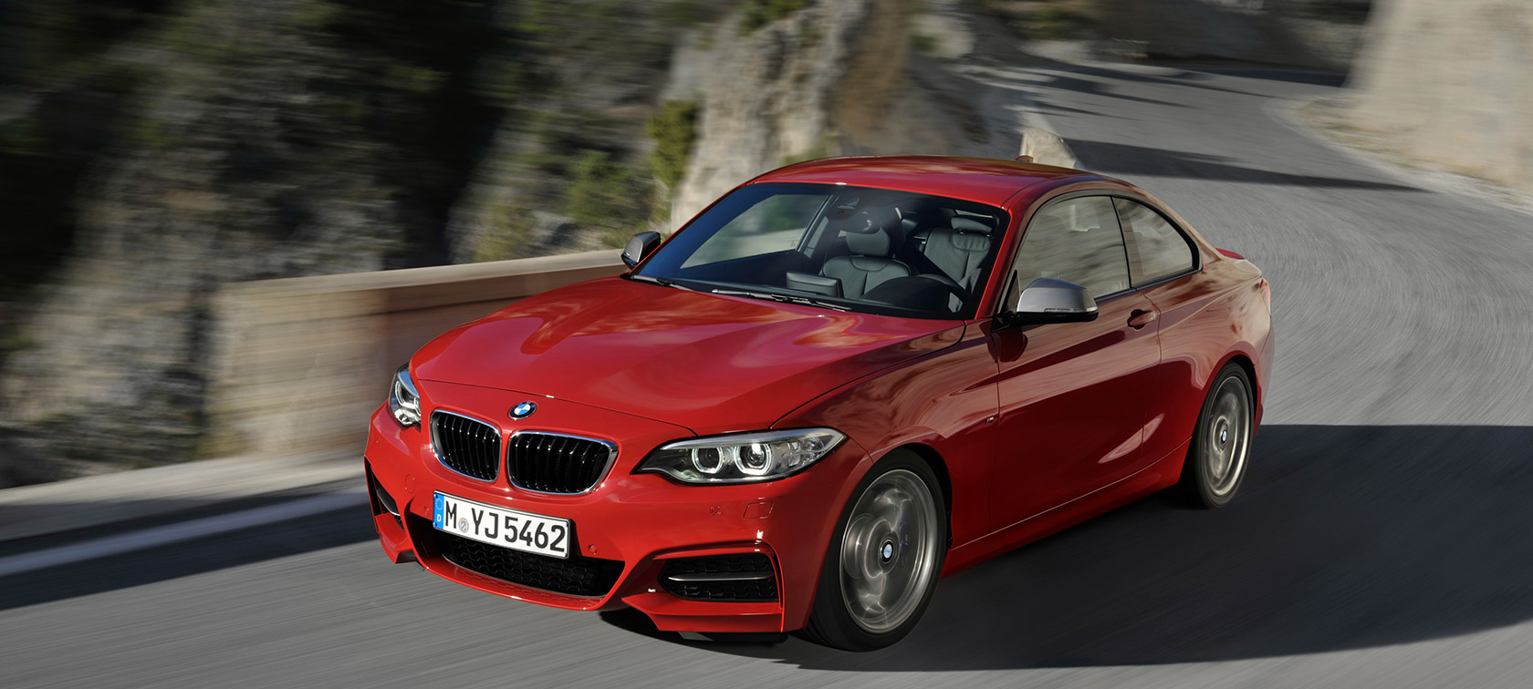 BMW 2 Series three-quarter front view driving on road in front of landscape BMW 2 Series BMW three-quarter front view driving on road in front of landscape