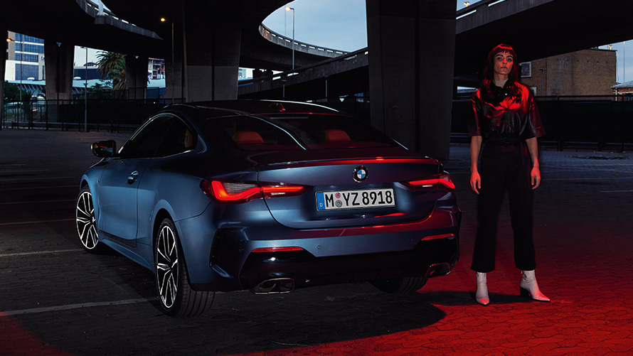 BMW 4 Series Coupé (G22), Artic Race Blue metallic, rear view with person BMW 4 Series Coupé (G22), Artic Race Blue metallic, rear view with person