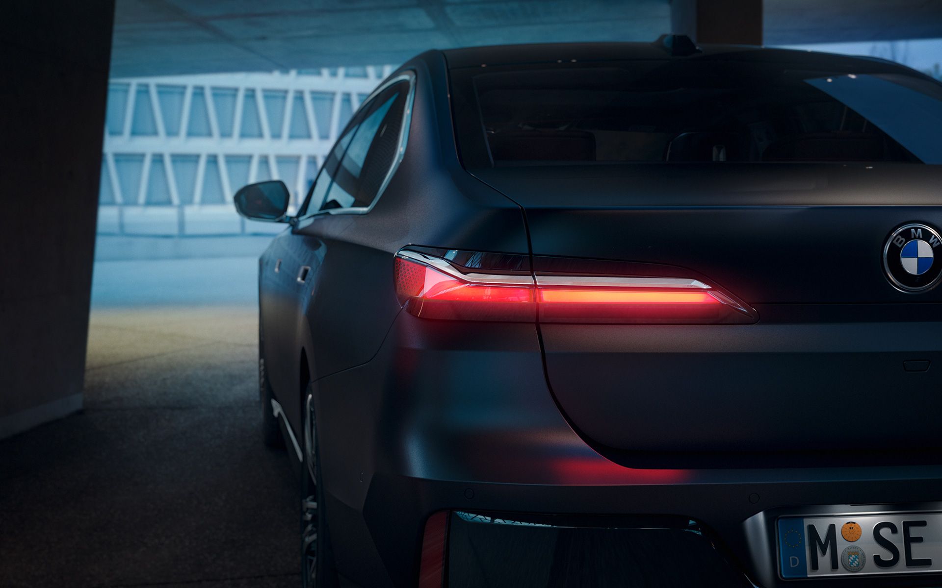 Rear view BMW 7 Series Sedan G70 ICE 740i M sports package Frozen Deep Grey metallic BMW 7 Series Sedan G70 ICE 740i M sports package Frozen Deep Grey metallic rear view with red glowing taillight in tunnel