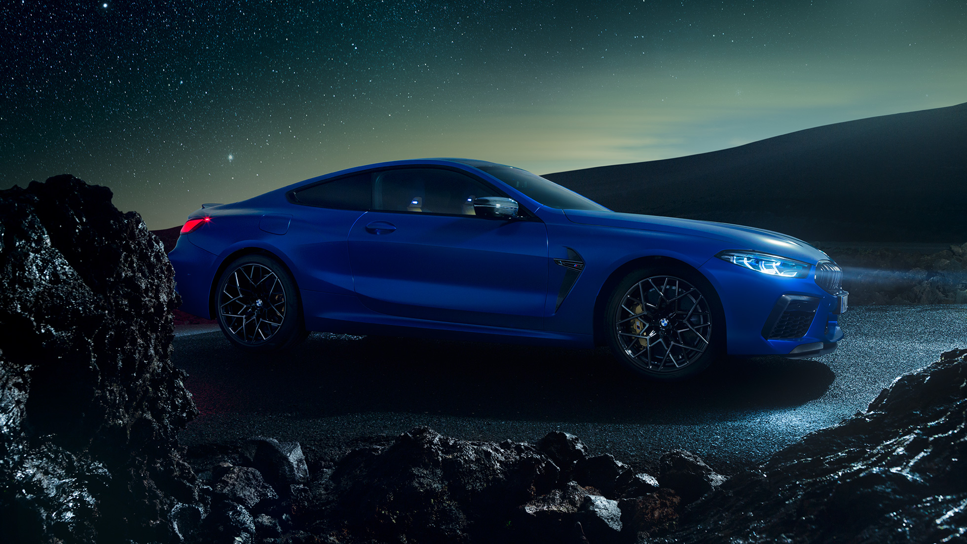 BMW M8 Coupé, three-quarter side view. BMW M8 Coupé in Marina Bay Blue metallic, standing three-quarter side view at night.