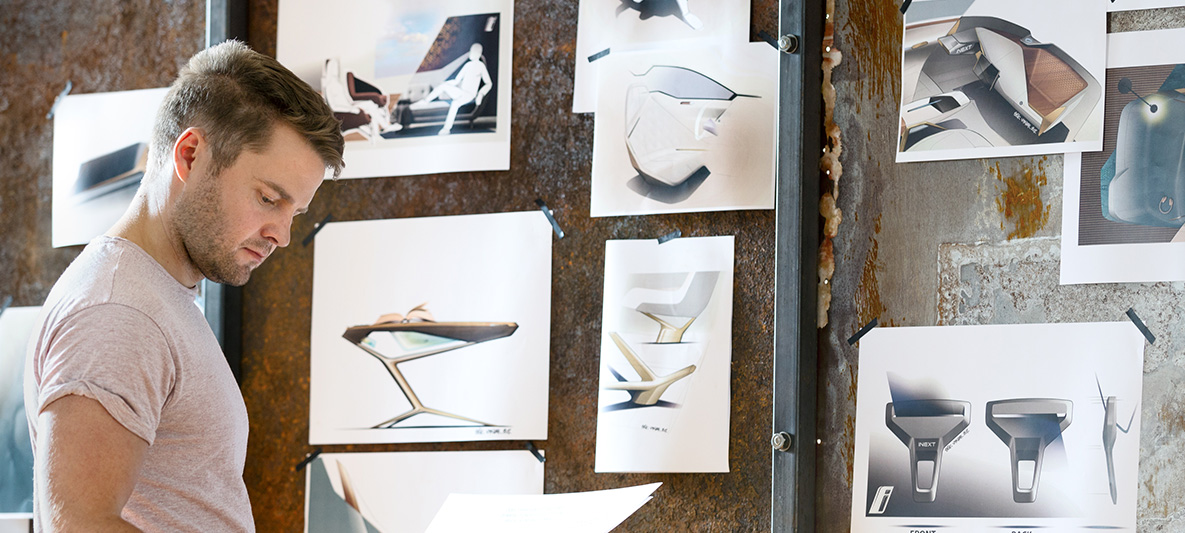 Skteches of the BMW Vision iNEXT Man in front of wall with sketches of the BMW Vision iNEXT