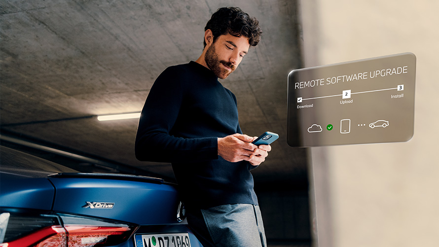 Man leaning against BMW rear and looking at his smartphone Remote Software Upgrade Man leaning against BMW rear and looking at his smartphone