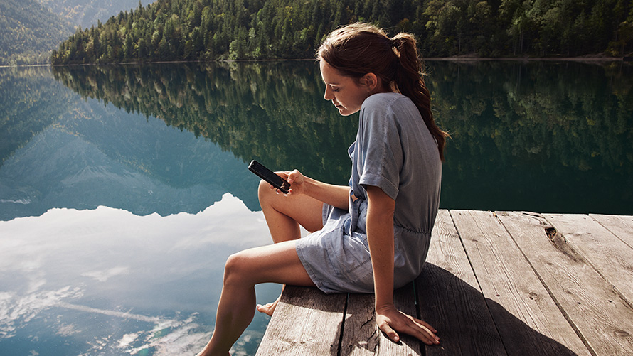 Woman sitting on a pier looking at her smartphone BMW Spring Summer Accessories Woman sitting on a pier looking at her smartphone