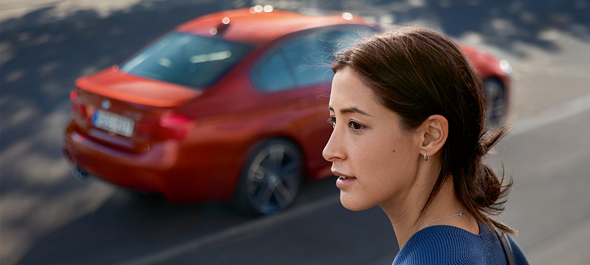 A woman looking into the distance. A BMW passes behind her. A woman looking into the distance. A BMW passes behind her.